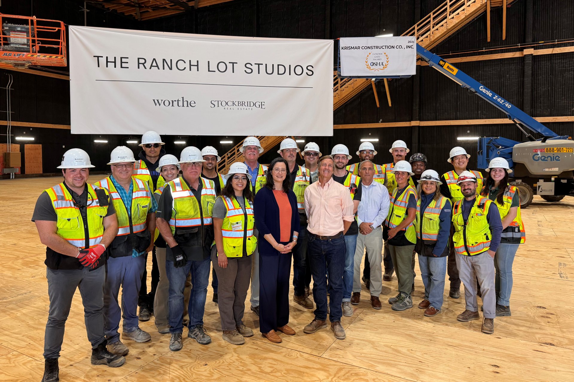 A group of about 20 people wearing hard hats and hi-vis vests pose for a group photo in front of a sign that says 'The Ranch Lot Studios'